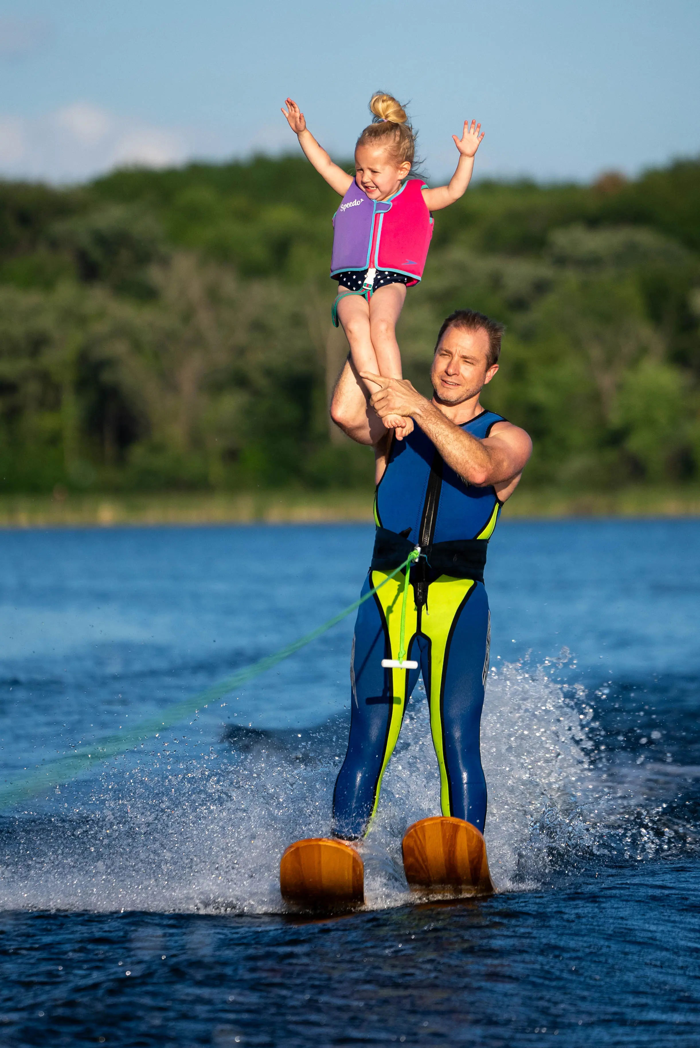 Father waterskiing while lifting young daughter overhead on Lake Minnewashta