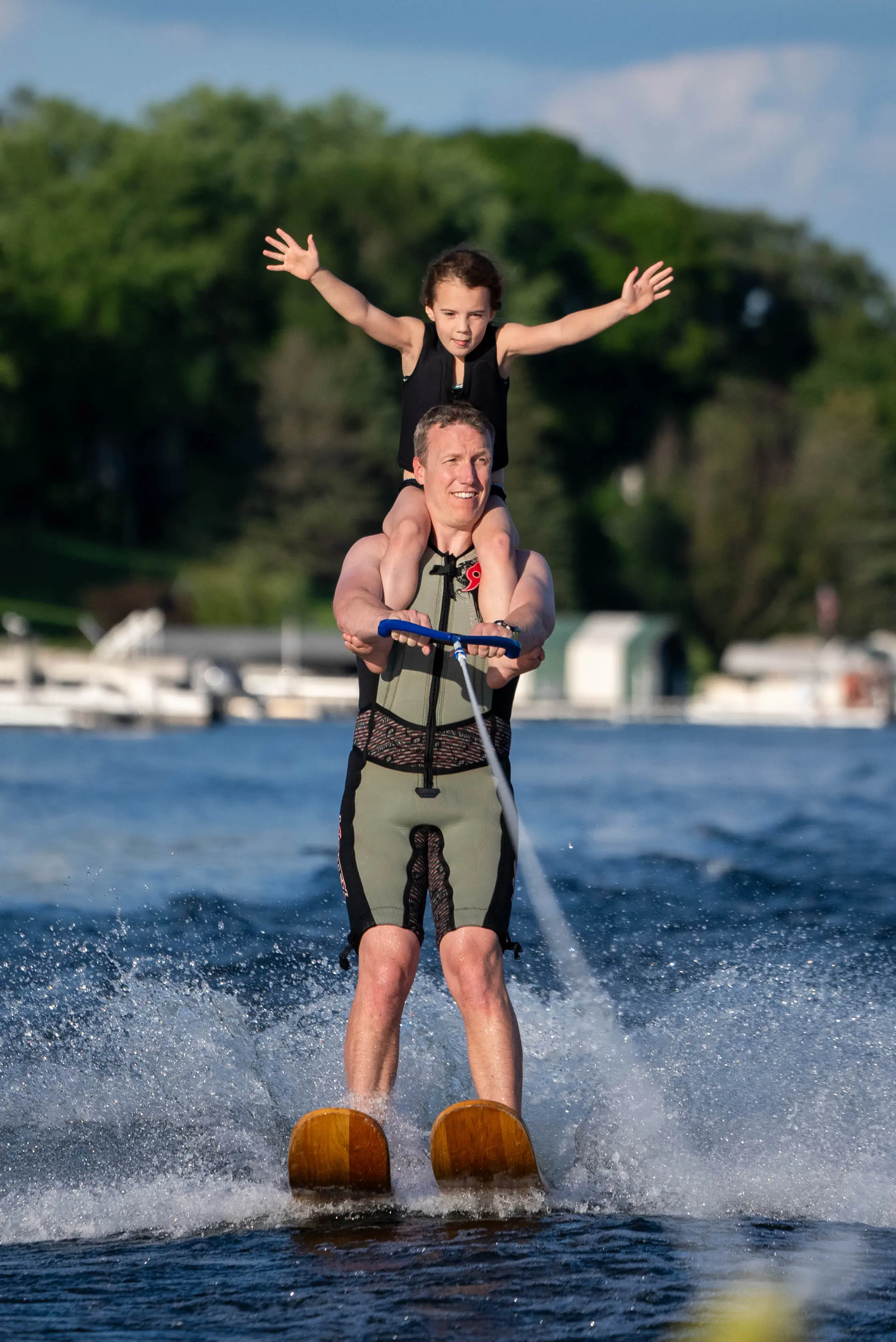 Father waterskiing with child on his shoulders, arms spread wide